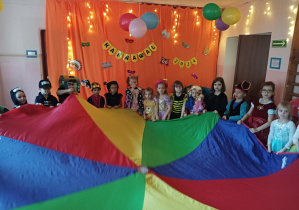 dzieci w przebraniach karnawałowych tańczą na balu przebierańców, na sali gimnastycznej, przy kolorowej chuście animacyjnej