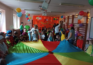 dzieci w przebraniach karnawałowych tańczą na balu przebierańców, na sali gimnastycznej, przy kolorowej chuście animacyjnej