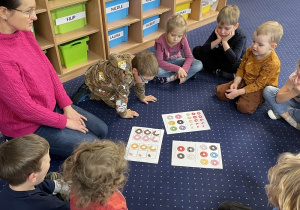 dzieci siedzą w kręgu na podłodze, przed nimi karty pracy z kolorowymi pączkami
