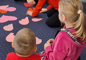 dzieci w czerwonych strojach bawią się papierowymi sercami