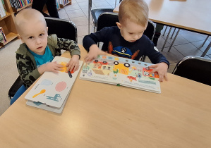 dwóch chłopców ogląda książki przy stoliku w bibliotece