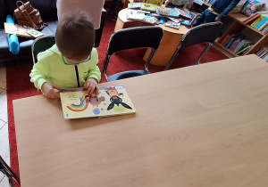 chłopiec ogląda książki przy stoliku w bibliotece