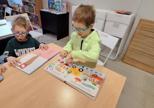 dwóch chłopców ogląda książki przy stoliku w bibliotece