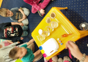 Dzieci siedzą na podłodze i obserwują eksperymenty.