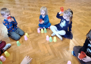 Dzieci siedzą na podłodze i układają kolorowe kubeczki.