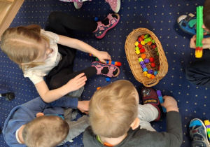 Dzieci siedzą na dywanie i układają klocki.