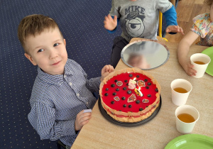 Dzieci siedzą przy stole. Przed chłopcem stoi tort.