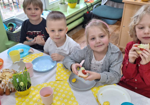 Dzieci siedzą przy stole i zjadają własnoręcznie wykonane kanapki wielkanocne.