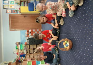 dzieci siedzą w kręgu na dywanie, na środku widać wielkanocny koszyczek z pisankami