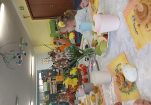 dzieci siedzą przy stolikach, na których ustawione są wielkanocne smakołyki