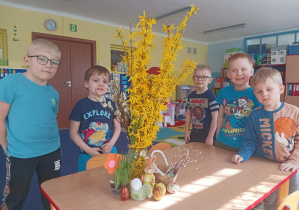 pięciu chłopców stoi przy stoliku, na którym ustawiony jest wazon z żółtymi kwiatami, ozdoby wielkanocne