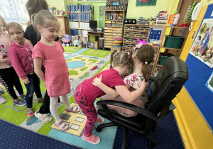 Dzieci podchodzą do dziewczynki na krześle i składają jej życzenia.