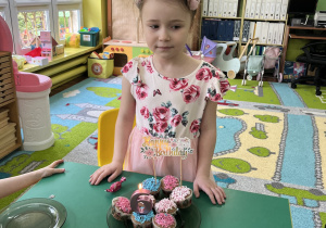 Dziewczynka stoi przed stołem na którym stoi tort.
