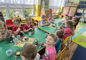 Dzieci siedzą przy stole i zjadają słodycze.