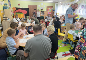 Rodzice i dzieci przy stolikach. Dzieci ozdabiają torebki na saszetki herbaty.