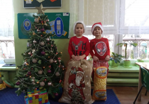 Dwaj chłopcy przebrani za Mikołajów stoją przy choince.