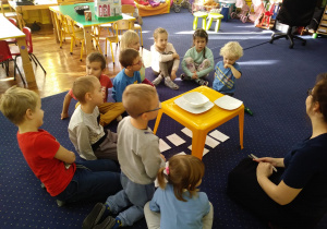 Dzieci słuchają informacji na temat właściwego ułożenia sztućców na stole i zachowania przy nim.
