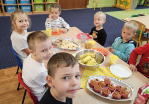 Dzieci siedzą przy stole na którym stoją słodkości.