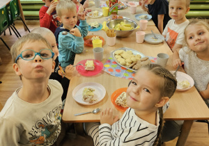 Dzieci siedzą przy stole na którym stoją słodkości.