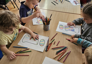 Dzieci siedzą przy stoliku i wykonują pracę plastyczną.