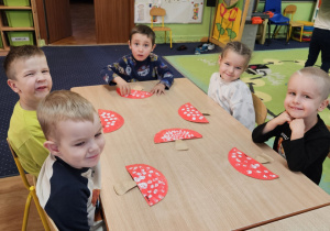 Dzieci siedzą przy stoliku i wykonują pracę plastyczną.