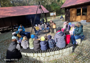 grupa dzieci siedzi dookoła paleniska, które znajduje się na środku podwórka