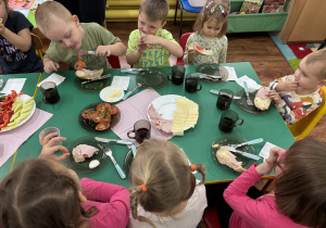 Dzieci siedzą przy stole i przygotowują sobie kanapki.