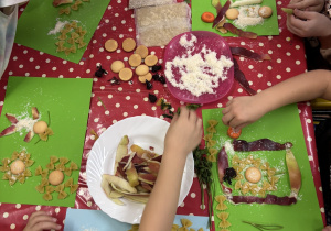 Dzieci siedzą przy stole i tworzą obrazy z produktów spożywczych.