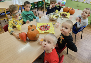 Dzieci siedzą przy stole na których leżą cukierki i dynie.