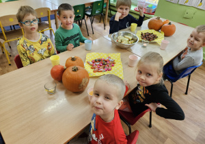 Dzieci siedzą przy stole na których leżą cukierki i dynie.