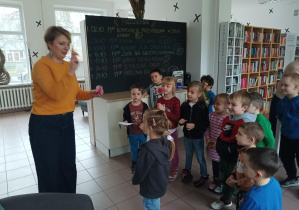 dzieci znajdują się w bibliotece, pani bibliotekarka wręcza dzieciom kartę biblioteczną