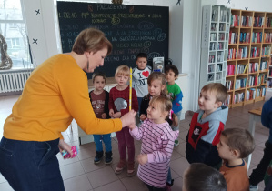 dzieci znajdują się w bibliotece, pani bibliotekarka wręcza dzieciom kartę biblioteczną