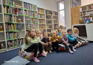 dzieci w bibliotece siedzą na dużych poduszkach i słuchają opowiadania