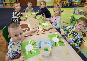 Dzieci siedzą przy stolikach i wykonują pracę plastyczną.