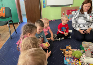 Dzieci siedzą w kole na dywanie i wykonują zadanie.