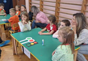 Dzieci siedzą przy stolikach i wykonują zadania.