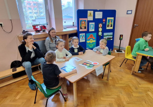 Dzieci siedzą przy stolikach i wykonują zadania.