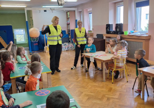 Dzieci siedzą przy stolikach i słuchają pani.