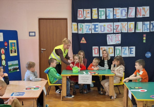 Dzieci siedzą przy stolikach i wykonują zadania.