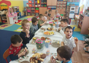 dzieci przy stolikach degustują słodycze, owoce, piją soki