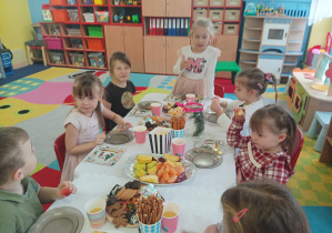 dzieci przy stolikach degustują słodycze, owoce, piją soki