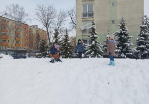 dzieci w zimowych ubraniach, bawią się na śniegu w ogródku przedszkolnym