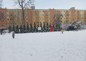 dzieci w zimowych ubraniach, bawią się na śniegu w ogródku przedszkolnym