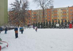 dzieci w zimowych ubraniach, bawią się na śniegu w ogródku przedszkolnym