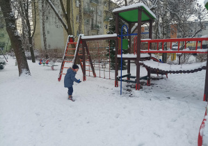 dzieci w zimowych ubraniach, bawią się na śniegu w ogródku przedszkolnym