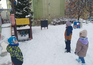 dzieci w zimowych ubraniach, bawią się na śniegu w ogródku przedszkolnym