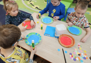 Dzieci wykonują pracę plastyczną przy stolikach.