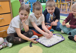 Dzieci siedzą na dywanie i oglądają sztuczny śnieg.