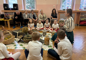 Dzieci siedzą na podłodze wokół zgromadzonych na podłodze ziół.