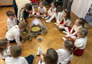 Dzieci siedzą na podłodze i obserwują panią.